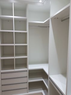 an empty walk in closet with white shelves and drawers on each side, along with no doors