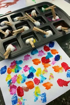 an art project with popsicle sticks and watercolors on paper next to a muffin tray