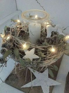 a candle is lit on top of a wreath with pine cones and evergreen leaves in the center