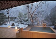 a hot tub sitting on top of a wooden deck next to a snow covered forest