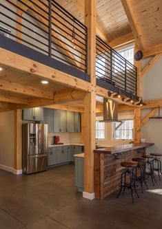 an open kitchen and living room area in a loft style home with wood beams, metal railings, and stainless steel appliances