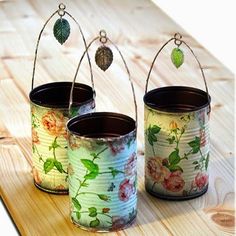 three tins with flowers painted on them are sitting on a wooden table and one is hanging from a wire