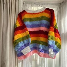 a multicolored sweater hanging on a window sill next to a white curtain