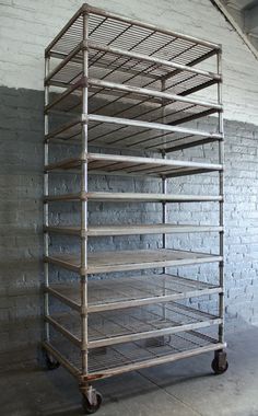 a metal rack with six shelves on wheels in front of a brick wall and floor