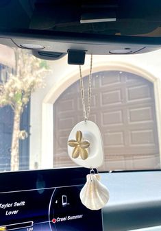 a car dashboard with a cell phone hanging from it's side window and a flower charm attached to the dash board