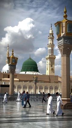 several people walking around in front of a large building with two green domes on top