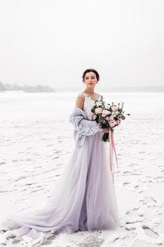 a woman standing in the snow holding a bouquet of flowers and looking at the camera