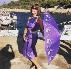 a woman in a purple dress is holding an umbrella near the water with other boats