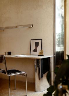 a desk with a chair and pictures on it in a room next to a plant