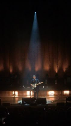 a man standing on top of a stage with a guitar in his hand and lights behind him