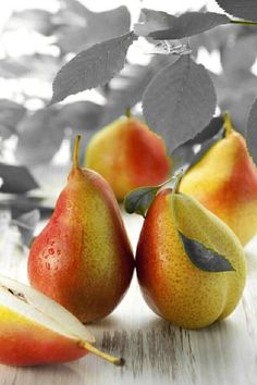 three pears and one apple on a wooden table with leaves in the back ground