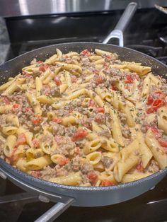 a skillet filled with pasta and meat on top of an oven burner next to a stove