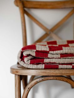 a stack of red and white blankets sitting on top of a wooden chair next to a wall