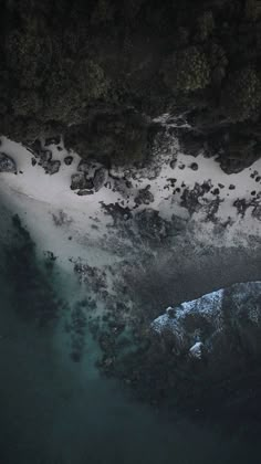 an aerial view of snow covered rocks, water and trees in the background at night