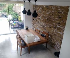 a wooden table sitting in front of a window next to a brick wall with lights hanging from it