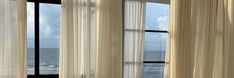 there is a window with curtains on it and the ocean in the backround