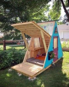 a dog sitting in the grass next to a small wooden structure with its door open