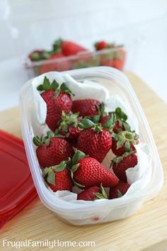 a plastic container filled with strawberries on top of a wooden cutting board