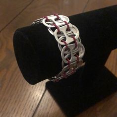 a silver bracelet with red stitching on top of a black velvet ring stand in front of a wooden floor