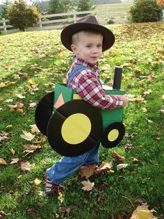 a young boy wearing a tractor costume in the grass with leaves on the ground around him