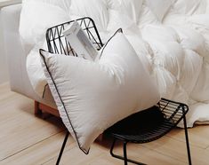 a white couch with two pillows on it and a black wire basket under the pillow