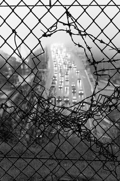 black and white photograph of traffic through a chain link fence at an overcast day