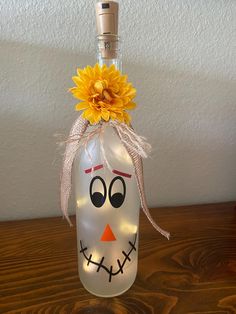 a bottle with a sunflower in it and a face painted on the top is sitting on a table