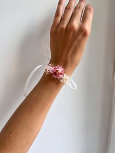 a woman's hand wearing a bracelet with pink flowers and white ribbon around it