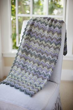 a crocheted blanket sitting on top of a white chair next to a window