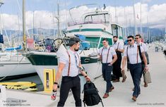 a group of men walking across a pier next to boats on the water and one man carrying a backpack