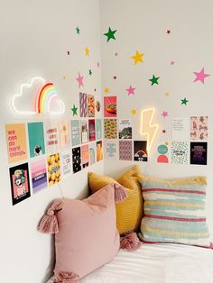 a white bed topped with lots of pillows next to a wall covered in pictures and neon lights