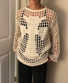 a woman standing in front of a door wearing a white crocheted sweater and black pants