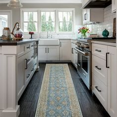 a kitchen with white cabinets and black counter tops, an area rug on the floor