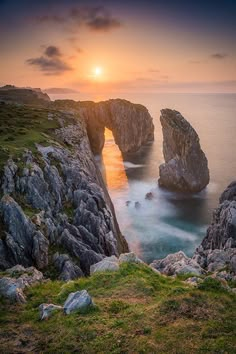 the sun is setting over an ocean with rocks