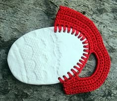 a crocheted red and white object laying on top of a stone slab next to a rock