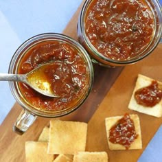 two jars filled with sauce and crackers on a cutting board