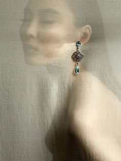 a woman's face is reflected in the glass behind her earring, while she wears a white dress