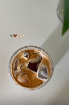 an iced drink with ice cubes in it on top of a white table next to a green plant