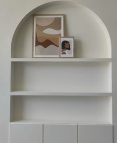 a white book shelf with two pictures on it and a framed painting above the shelves