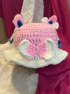 a pink and white crocheted hat with an elephant on the front, sitting on a bed