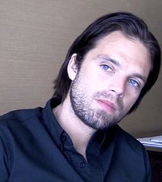 a man with long hair and blue eyes sitting in front of a laptop computer looking at the camera