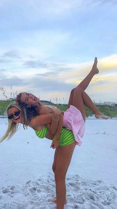 a woman on the beach with her leg in the air while holding onto another woman's back