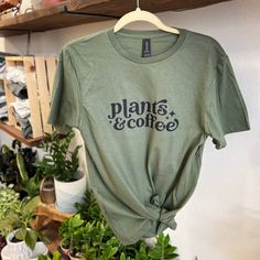 Dark Moss Green Tee With Plants & Coffee Graphic. 100% Cotton. Available In S-Xl. Casual Coffee Colored Everyday Tops, Casual Coffee Colored Top For Everyday, Trendy Coffee-colored Relaxed Fit Top, Relaxed Fit Coffee Color Tops For Fall, Trendy Coffee Relaxed Fit Top, Trendy Relaxed Fit Coffee Top, Summer Coffee Colored Tops With Graphic Print, Coffee Color Graphic Print Summer Top, Coffee Graphic Print Tops For Summer