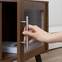 a person is opening the door to a wooden cabinet with glass inserts on it