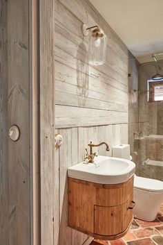 a bathroom with a sink, toilet and wooden paneling on the wall behind it