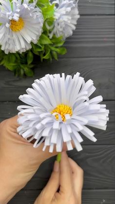 someone is holding a paper flower in front of some white daisies on a table