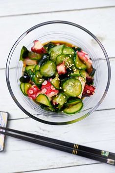 a glass bowl filled with cucumber and other vegetables next to chopsticks