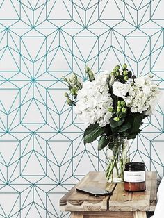 a vase filled with white flowers sitting on top of a wooden table next to a wall