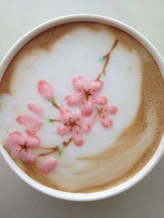 a white cup filled with liquid and pink flowers on top of it's side