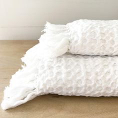 two white towels folded on top of each other in front of a wooden table and wall